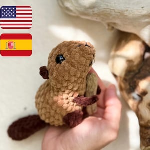 May include: A brown crocheted beaver plush toy with black eyes. The toy is being held in a person's hand.