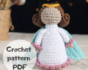 Könnte beinhalten: Häkelanleitung PDF für eine kleine Engel-Amigurumi-Puppe. Die Puppe hat braunes Haar, ein weißes Kleid mit rosa Besatz und einen hellblauen Umhang.