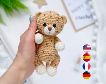 May include: A crocheted cheetah plush toy with brown spots, white paws, and black eyes. The toy is being held by a hand.