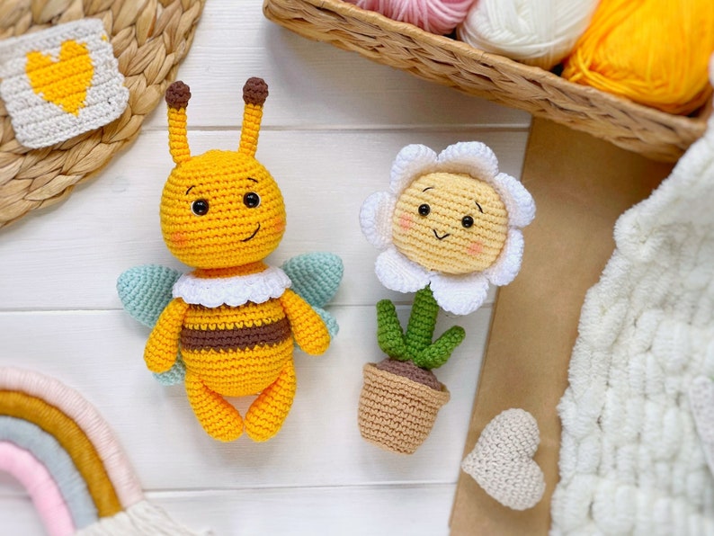 May include: A crocheted yellow bee with brown stripes and a white collar, and a crocheted white daisy with a yellow center and green stem in a brown pot.