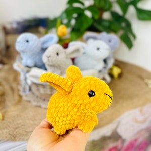 Puede incluir: Un conejito de crochet amarillo con ojos negros. El conejito est&aacute; sentado en una mano.