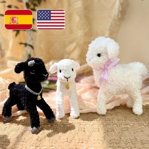 May include: Three handmade crochet lamb figurines. One is black with a silver chain and bell, another is white with a gold bell, and the third is white with a pink ribbon. The lambs are standing on a light brown surface.