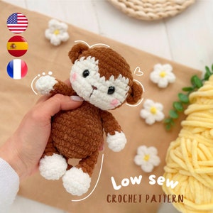 Puede incluir: Un juguete de mono amigurumi tejido a crochet con pelaje marrón y pies blancos. El juguete está siendo sostenido por una mano y está sobre una superficie marrón con flores blancas. El texto "Low sew CROCHET PATTERN" es visible en la imagen.
