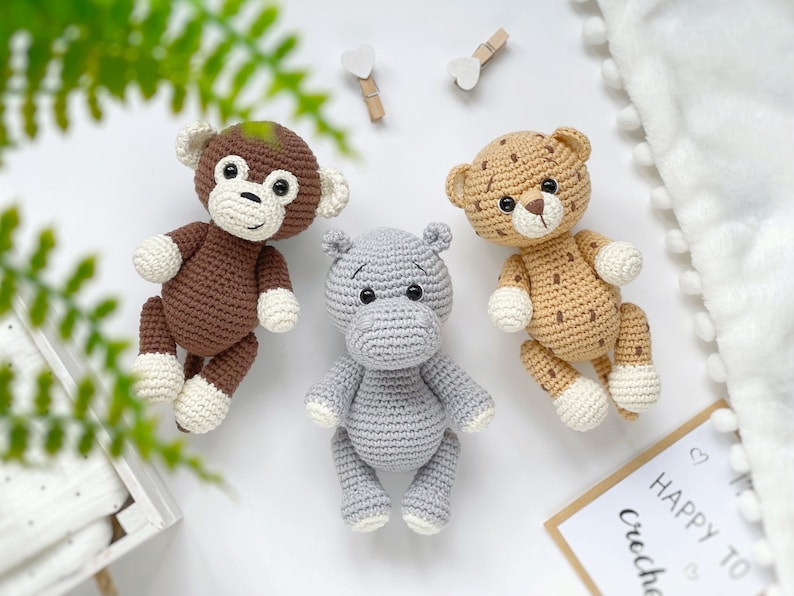 Op de afbeelding: Drie handgemaakte gehaakte knuffels, waaronder een bruine aap met witte pootjes, een lichtgrijs nijlpaard en een beige luipaard met donkerbruine vlekken en witte pootjes. Elk dier is voorzien van zwarte veiligheidsoogjes en stiksels.