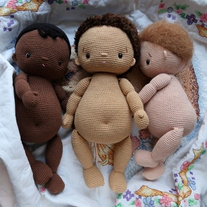 以下が含まれることがあります： 白い花柄の刺繍が施された白い編み物の毛布の上に、茶色、薄い茶色、ピンクの3体の編みぐるみ人形が横たわっています。