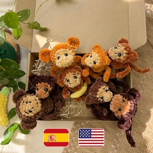 Pode incluir: Uma coleção de seis pequenos peluches de macaco feitos de crochê com fio macio e texturizado em vários tons de castanho e bege. Os macacos estão dispostos dentro de uma caixa de cartão, com um deles a segurar uma pequena banana amarela.