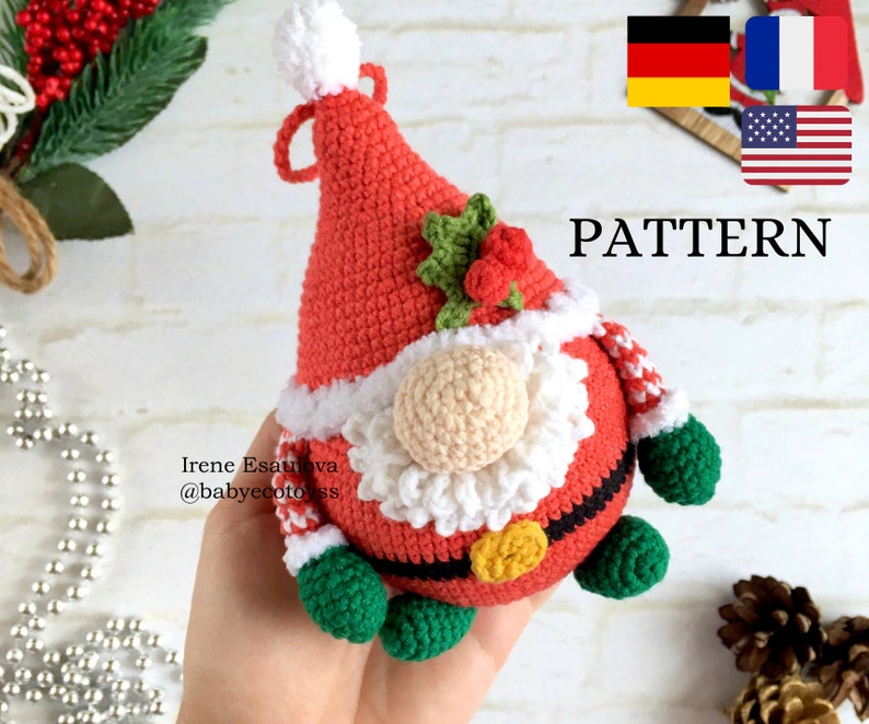 Pu&ograve; includere: Ornamento a forma di gnomo di Babbo Natale all'uncinetto. Lo gnomo ha un cappello rosso con pompon e finiture bianche, barba beige e corpo rosso con finiture bianche. Le braccia e i piedi dello gnomo sono verdi. La parola "PATTERN" &egrave; visibile.