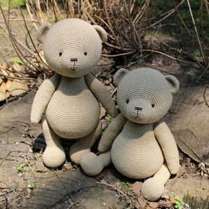 Peut inclure: Deux ours en peluche au crochet beiges sont pr&eacute;sent&eacute;s &agrave; l'ext&eacute;rieur. Les ours ont des yeux et des nez noirs et sont assis sur une souche d'arbre. Les ours sont faits d'un fil doux et textur&eacute; et ont une forme classique d'ours en peluche.