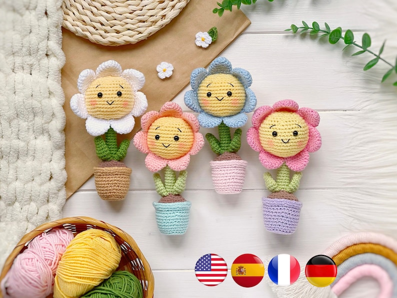May include: Four crocheted flower pot toys with smiling faces. The flowers are yellow, pink, blue, and white. The pots are brown, light blue, pink, and purple.