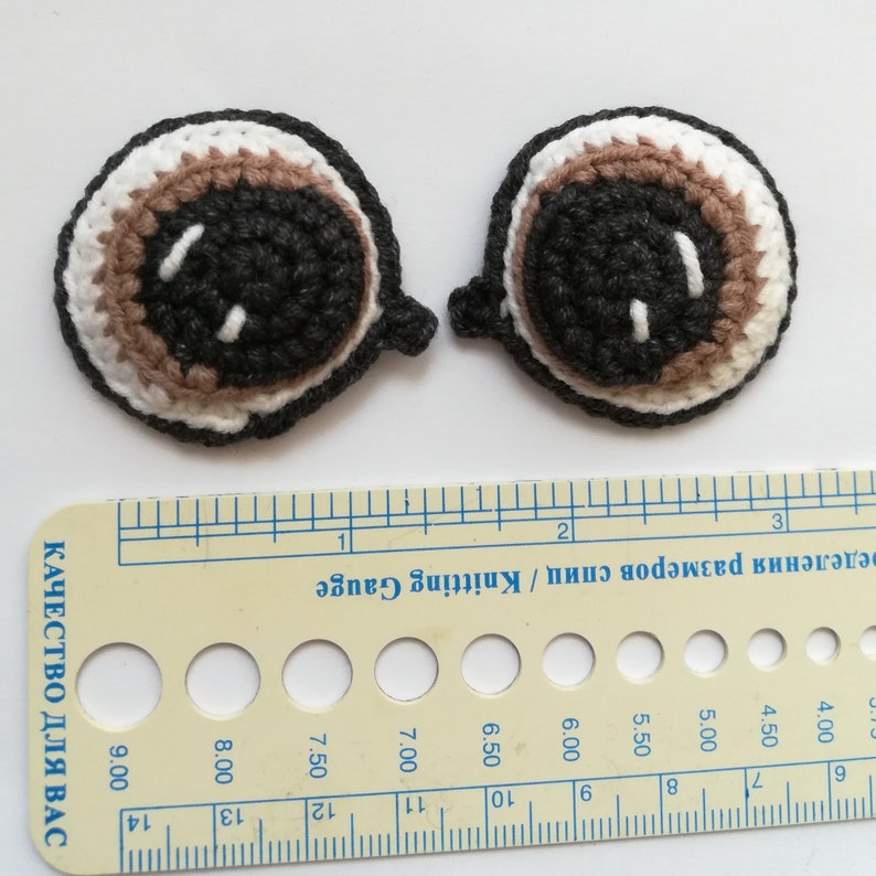 May include: Two crocheted eyes with brown, white, and gray yarn. The eyes are about 1 inch in diameter.