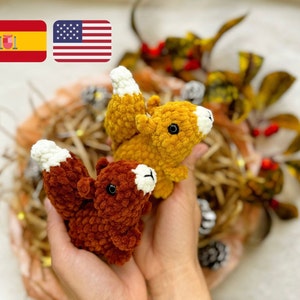 Może przedstawiać: Dwie pluszowe wiewiórki wykonane na szydełku, jedna brązowa, a druga żółta, są trzymane w dłoniach osoby. Wiewiórki mają białe akcenty z włóczki na ogonach i twarzach. Tło stanowi brązowy i żółty pleciony kosz.