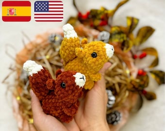 Puede incluir: Dos peluches de ardilla de crochet, uno marrón y otro amarillo, se sostienen en las manos de una persona. Las ardillas tienen detalles de hilo blanco en sus colas y caras. El fondo es una cesta tejida marrón y amarilla.