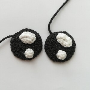 May include: Two black crocheted circles with white crocheted spots. The circles are connected by a black string.