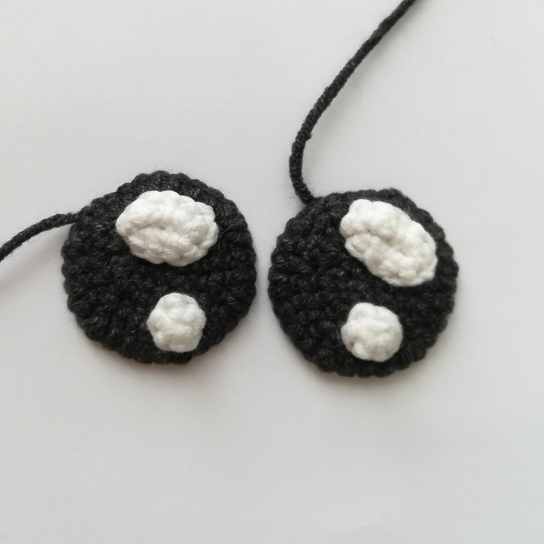 May include: Two black crocheted circles with white crocheted spots. The circles are connected by a black string.