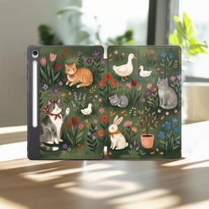 May include: A dark-edged tablet case featuring a green garden illustration with cats, a rabbit, ducks, and colorful flowers. The case includes a side slot holding a white stylus. The artwork depicts various animals nestled among tulips and foliage.