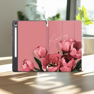 May include: Pink iPad case with a floral tulip design. The case is open, revealing the interior and a stylus. The cover features the name "Audrey" in cursive script, and a bouquet of pink tulips.