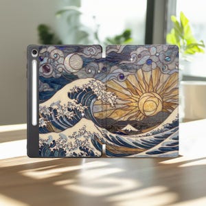 May include: A tablet case featuring a stained glass style design of a large ocean wave, a golden sun, and a crescent moon. The case is black with a side slot holding a white stylus. The artwork displays deep blue, cream, and gold tones.