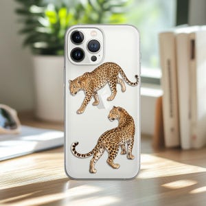 May include: A clear smartphone case featuring two detailed illustrations of leopards with golden-brown fur and black rosettes. The top leopard is walking forward, while the bottom leopard is positioned looking back over its shoulder.
