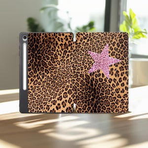 May include: A tablet case featuring a brown and black leopard print pattern across the entire surface. A large, five-pointed star with a pink and black leopard print design is centered on the right side. A white stylus is docked on the left side.