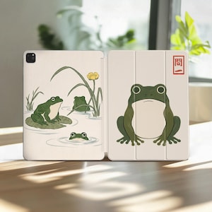 Puede incluir: Una funda para tableta de color claro con una ilustración impresa de ranas verdes en un estanque en el panel izquierdo y una gran rana verde en el derecho. El panel derecho incluye un sello rojo rectangular con el texto japonés 問一.