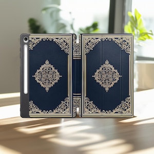 May include: A navy blue tablet case with a gold ornate design. The case is open, revealing the interior. A stylus is attached to the side. The design is reminiscent of a classic book cover.