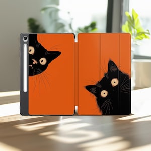 May include: A tablet case with a bright orange background featuring two black cat faces peeking from the corners. The case has a dark gray frame and a white stylus pen attached to the side. The design shows the cats with wide, light-colored eyes.