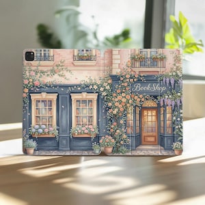 May include: A tablet case featuring a watercolor illustration of a quaint bookstore. The design showcases a building with blue trim, flower boxes, and the text "BookShop". The artwork is in soft pastel colors.