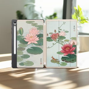 May include: A tablet case featuring a Japanese-style illustration of pink lotus flowers, green lily pads, and a dragonfly on a light blue background. The case includes a dedicated slot for a stylus pen and displays traditional calligraphy text.