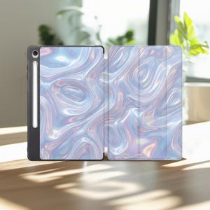 May include: A tablet case featuring a holographic, liquid-like swirl pattern in shades of light blue, silver, and iridescent pink. The case includes a dedicated vertical slot on the left side for a stylus, with a white stylus resting inside.