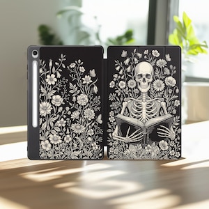 May include: A black tablet case featuring a white line art illustration of a skeleton reading a book surrounded by various wildflowers and butterflies. The case includes a dedicated slot for a stylus pen on the left side of the cover.
