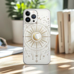 Könnte beinhalten: Transparente Handyhülle mit einem goldenen Sonnen- und Halbmond-Design. Die Hülle zeigt Sternbilder und himmlische Elemente. Die Handyhülle liegt auf einer Holzoberfläche.