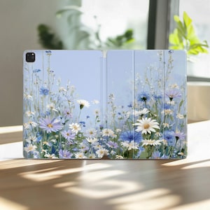 Op de afbeelding: Een lichtblauwe tablethoes met een bloemenpatroon van witte, blauwe en paarse bloemen. De hoes is open en toont de binnenkant en een gedetailleerd wildbloemenontwerp.