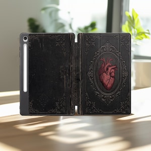 May include: Black tablet case with a vintage book design. The case is open, revealing a detailed illustration of a human heart within an ornate frame. The case has a stylus holder on the side.