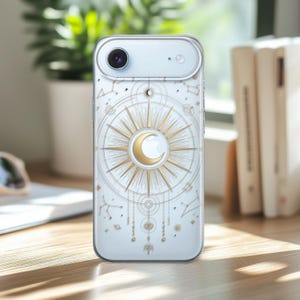 May include: Transparent phone case with a celestial design. It features a gold sunburst, crescent moon, and constellation details. The design is set against a clear background, with a silver camera and flash.