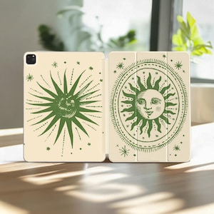 May include: An open tablet case with a cream-colored background. The case features a green sun design on both sides. The sun design has a face in the center and is surrounded by rays and stars. The case is on a wooden surface.