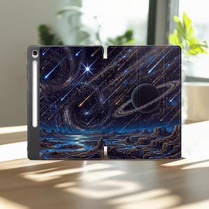 May include: A black tablet case featuring a vibrant space scene with a dark planet surrounded by rings, swirling galaxies, and bright streaks of falling stars above a rocky, blue-tinted landscape. A white stylus is attached to the side of the case.