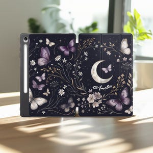 May include: A black tablet case with a butterfly and floral design. The case features purple and white butterflies, white flowers, and the name "Amelia" on the cover. A stylus is attached to the side.