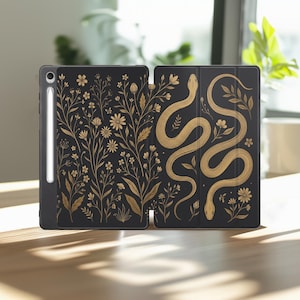 May include: A black tablet case featuring a gold-colored botanical print of wildflowers on the left panel and a winding snake intertwined with floral stems on the right panel. A white stylus is attached to the side of the tablet case.