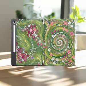 Può includere: Una custodia per tablet con sfondo verde, un design a spirale dipinto e fiori rosa e bianchi sparsi. La custodia include uno slot dedicato per una penna stilo bianca sul lato sinistro, che mostra un motivo floreale dettagliato.
