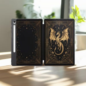May include: A black tablet case featuring a gold-colored dragon illustration on the right panel, surrounded by floral motifs and crescent moons. The left panel displays a matching gold-colored ornate border with stars, and a stylus is attached to the side.