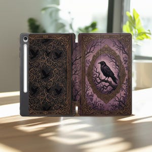 May include: A tablet case featuring a black and gold filigree pattern with silhouettes of flying crows on the left panel and a central oval frame containing a black crow perched on a branch against a purple background on the right panel.