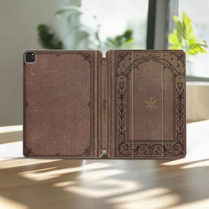 May include: A brown tablet case featuring a dark brown decorative border with floral motifs and a central gold snowflake icon. The design mimics an antique book cover with intricate line work, corner flourishes, and a textured appearance.