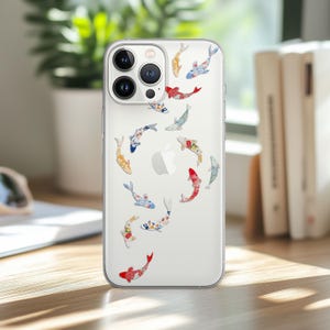 May include: Clear iPhone case adorned with colorful koi fish designs. The fish feature patterns in red, blue, yellow, and white. The case has a clear back and a camera bump.