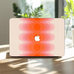 May include: A laptop with a retro-style design. The cover features a wavy pattern in shades of orange and pink, with a white Apple logo in the center. The laptop is on a wooden surface.