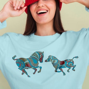 May include: Machine embroidery design featuring two stylised zebras in blue, green, red, and brown colours. The design is shown on a light blue sweatshirt. The file formats available are DST, EXP, HUS, JEF, PES, and VP3.
