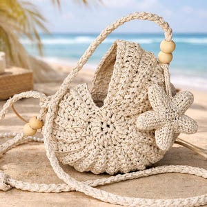 May include: A cream-colored, crocheted handbag with a starfish accent, set on a sandy beach. The bag features a braided handle and strap, with wooden bead details. The ocean and palm trees are in the background.