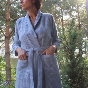 May include: A light blue waffle weave robe with a shawl collar and a tie belt. The robe has two pockets on the front.