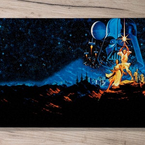 May include: A black and blue Star Wars poster featuring Darth Vader, Luke Skywalker, and Princess Leia. The poster has a dark blue background with stars and a distant planet. The characters are standing on a rocky surface with a cityscape in the background.