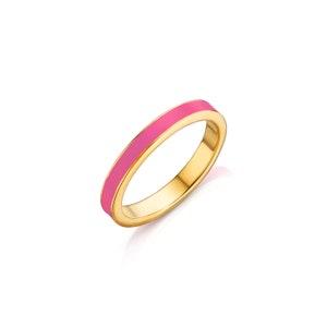 Puede incluir: Un anillo de oro con una banda de esmalte rosa brillante. El anillo está sobre un fondo blanco, resaltando su superficie pulida y reflectante. La banda es de un color vibrante y sólido, creando un contraste llamativo con el oro.