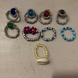 May include: A collection of eight beaded rings with various colors and designs, including a ring with a seashell charm.